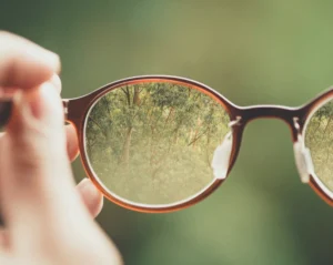 Man sieht den Blick durch eine Brille, die ein Mensch ca. 40 cm vor sich hält. Das ist eine Matapher dafür, dass Glaubenssätze und Denkmuster unsere Wahrnehmung wie eine Brille beeinflussen.