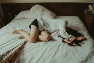 Frau liegt am Bett, den Arm über den Kopf gelegt.